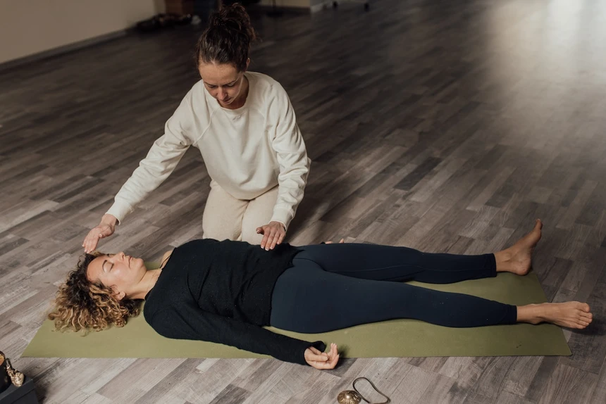 Practicante de energía curando a una mujer relajada en una alfombra de yoga